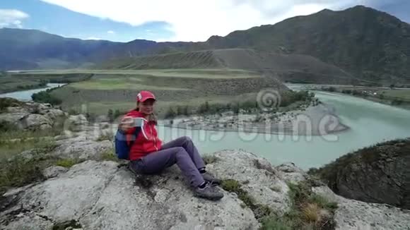年轻的女游客坐在石头上在智能手机上拍照美丽的山和蓝色的山视频的预览图