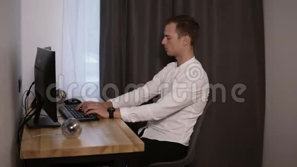年轻人自由职业者在家工作坐在办公桌前用鼠标在键盘上打字穿着白衬衫的人很放松视频的预览图