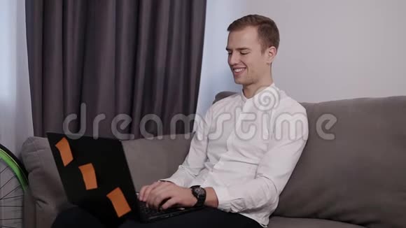 放松微笑的年轻人坐在沙发上在家里工作用笔记本电脑心情愉快自由职业者带现代化房间视频的预览图
