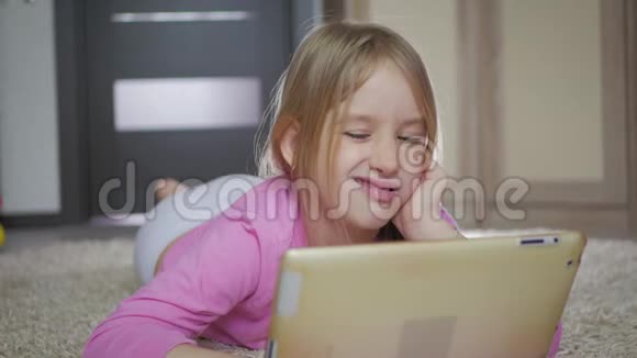 快乐的小女孩玩平板电脑电脑躺在家里的地板上视频的预览图