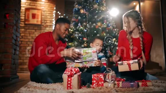 新年礼物中一个幸福的家庭正坐在圣诞树附近这个男孩拿着最大的礼物视频的预览图