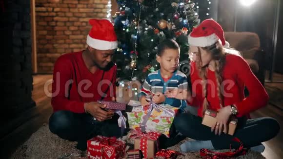 新年礼物中一个幸福的家庭正坐在圣诞树附近这个男孩正在解开最大的礼物视频的预览图