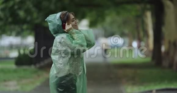 雨天年轻的女人在公园里跳舞听耳机里的音乐4k视频的预览图