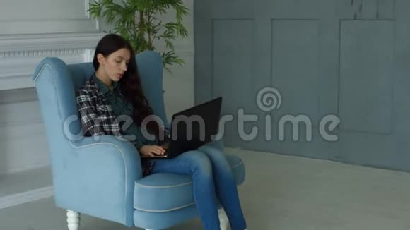 优雅的女士在扶手椅上通过笔记本电脑在线聊天视频的预览图
