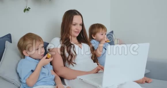 漂亮的年轻妈妈和两个小男孩正在看手提电脑屏幕的家庭照片他们在网上购物视频的预览图