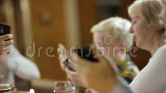 长发男子在圣诞家庭餐桌上向祖母展示他的智能手机屏幕视频的预览图