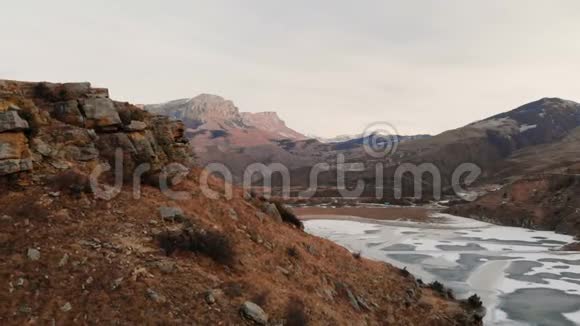 以史诗般的岩石和悬崖为背景在冻结的山湖畔鸟瞰山坡和悬崖视频的预览图