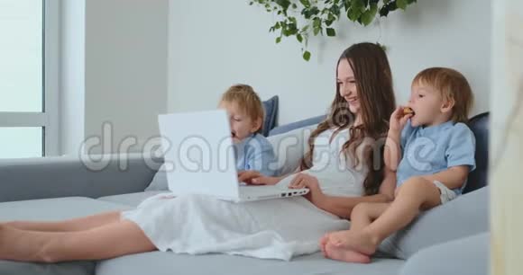 漂亮的年轻妈妈和两个小男孩正在看手提电脑屏幕的家庭照片他们在网上购物视频的预览图