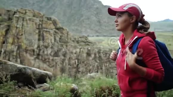 旅行者女孩戴着帽子背着背包爬山特写镜头背景山脉和河流视频的预览图