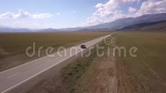 一辆灰色汽车沿着公路穿过平坦的田野的空中景色在背景上升的斜坡视频的预览图