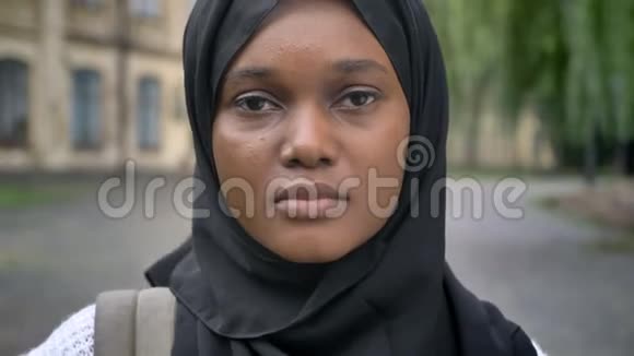 悲伤的年轻非洲穆斯林妇女戴着头巾看着摄像机站在大学附近的公园里严肃而关切视频的预览图
