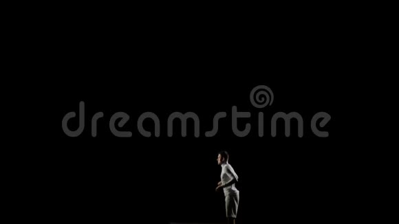 穿着白色衣服的黑色背景上的男体操从下面开始进入框架在空中旋转视频的预览图
