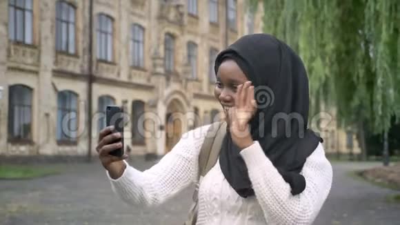 年轻的非洲穆斯林学生戴着头巾通过电话视频聊天站在大学附近的公园里快乐和快乐视频的预览图