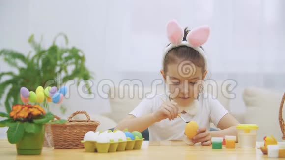 一个顽皮的小女孩头上戴着小兔子的耳朵正选择红色来画一个鸡蛋平静地在画画视频的预览图