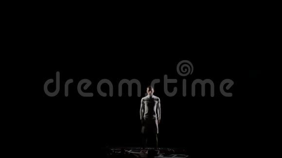 穿着白色衣服的黑色背景上的男体操从下面开始进入框架在空中旋转视频的预览图