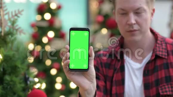 圣诞快乐青年在发光的圣诞树户外展示电话视频的预览图