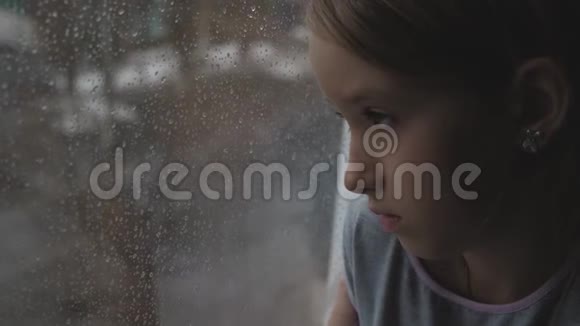 伤心的少年女孩在雨天透过窗户看着外面视频的预览图