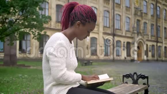 年轻的非洲女学生坐在长凳上在大学附近的公园看书准备上课视频的预览图