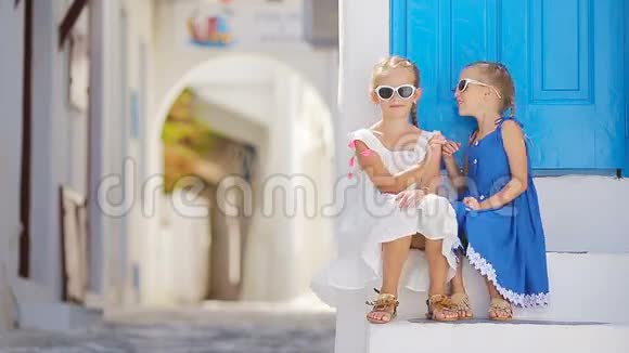 可爱的小女孩在典型的希腊传统村庄的街道白色的墙壁和五颜六色的门在米科诺斯岛视频的预览图