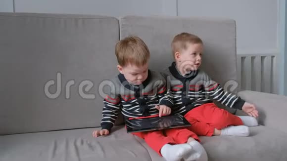 两个孪生兄弟坐在沙发上平板带走了对方孩子们在平板电脑上玩游戏视频的预览图