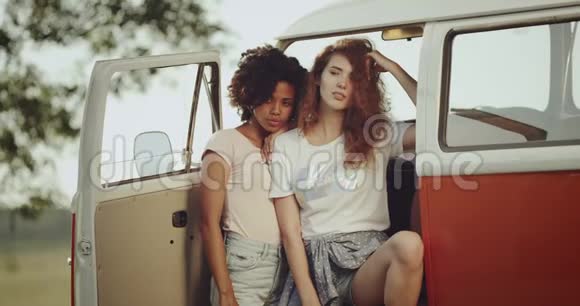 两位年轻漂亮的女士摆姿势拍照脸严肃她们站在复古橙色的公共汽车旁视频的预览图