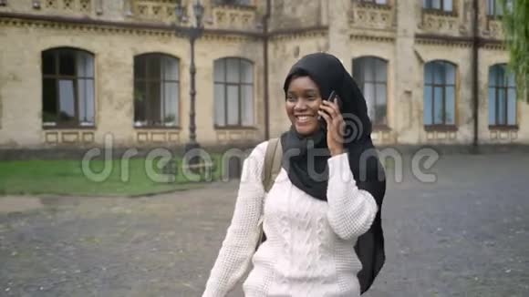 美丽的穆斯林非裔美国女学生头戴头巾离开大学用手机说话视频的预览图