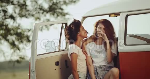 非洲和红头发的女孩有着良好的心情微笑和度过了一段美好的时光坐在复古橙色的公共汽车前视频的预览图