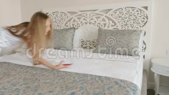 快乐的青少年女孩智能手机躺在家里的卧室的白色床上年轻的少女放松手机视频的预览图