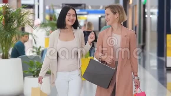 慢动作两个漂亮的女人在购物中心散步看商店在大庭广众之下嘲笑女孩视频的预览图