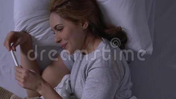 幸福的女人躺在床上看着验孕结果阳性视频的预览图