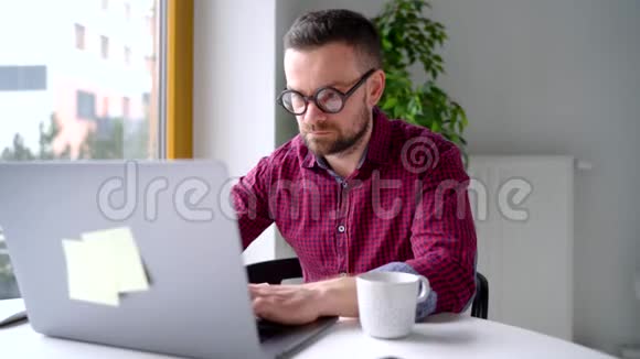 戴眼镜的胡子男坐在家里的办公室用笔记本电脑工作视频的预览图