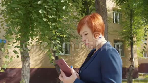 漂亮的红发女人一边看手机一边看视频的预览图