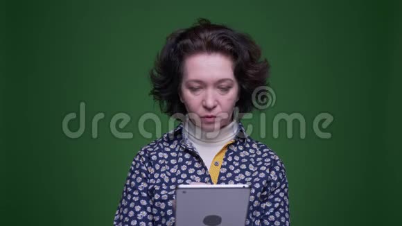 用平板电脑拍摄白种人深色头发的老女性的特写肖像背景是绿色的视频的预览图