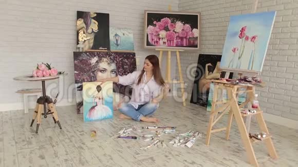 一位才华横溢的女艺术家坐在地板上他的许多画中视频的预览图