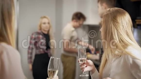 带着香槟酒杯的年轻人在厨房里交谈和准备视频的预览图