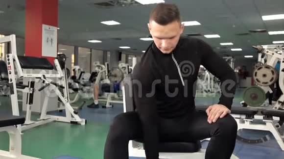 年轻肌肉发达的运动员在健身房锻炼坐在举重机上举起两个哑铃视频的预览图
