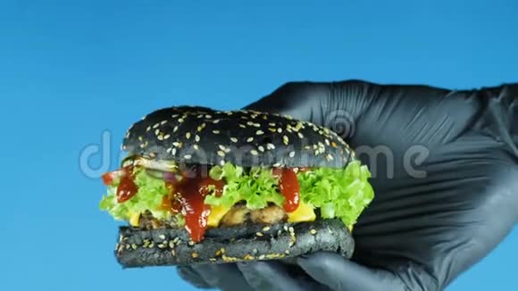 汉堡特写镜头厨师戴着黑手套展示一个汉堡里面有黑面包生菜叶和番茄酱视频的预览图