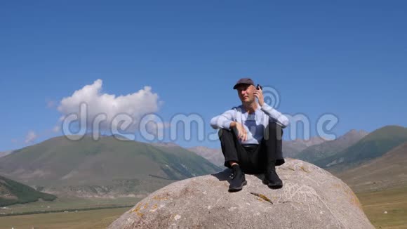 一个人坐在石头上打电话身后是天山视频的预览图