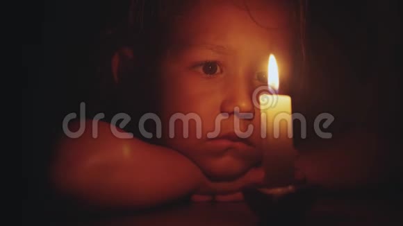描绘一个小可爱的女孩她坐在黑暗中看着燃烧的蜡烛视频的预览图