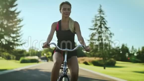 阳光明媚的一天运动妇女骑自行车在城市公园骑自行车快乐视频的预览图