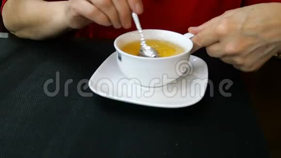 女人手在一个白色的陶瓷杯里搅拌热的新鲜茶视频的预览图