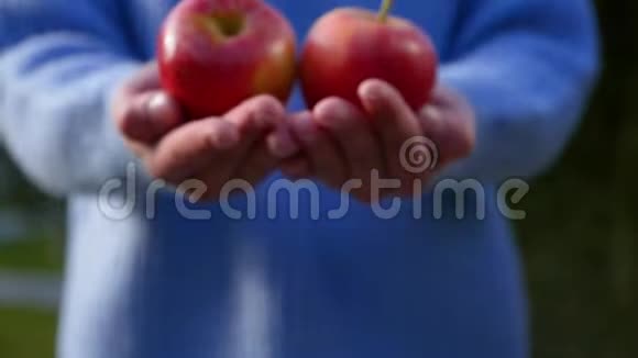 一位身材矮小的年轻女子用成熟的红苹果把手伸向照相机视频的预览图