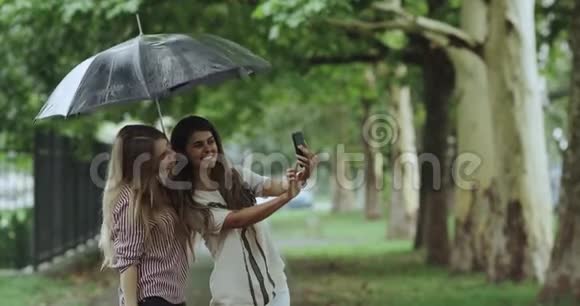 下雨天两位漂亮的年轻女士在伞下自拍视频的预览图