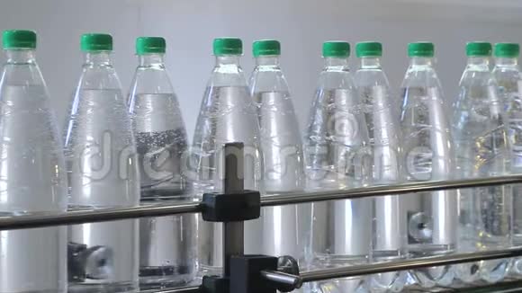白色塑料瓶站在装瓶线上装满矿泉水用绿色的瓶盖堵塞视频的预览图