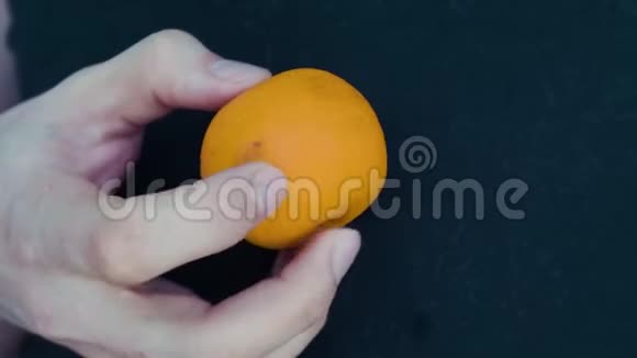 特写的手手中的橘子在黑色的背景上扭动视频的预览图