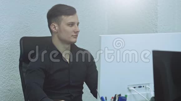 有魅力的年轻人在他的工作场所使用电脑办公室工作人员微笑着看着摄像机视频的预览图