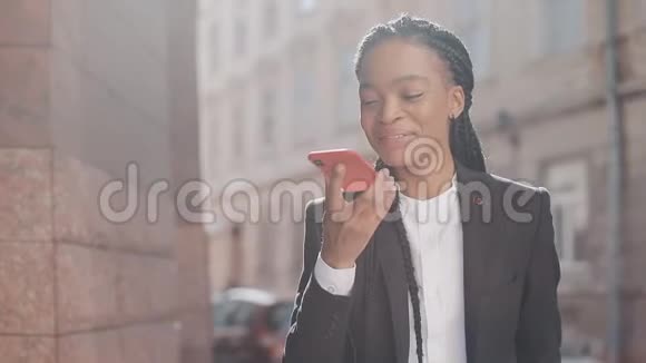 时尚的非洲商务女性在户外与手机助手交谈时用手机发送音频语音信息商务视频的预览图