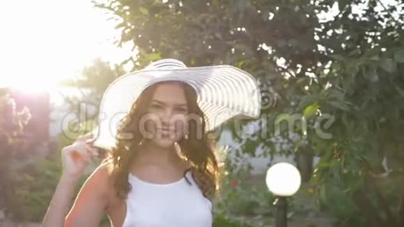 快乐的女孩戴着宽边白帽子在慢动作的太阳能照明中调情视频的预览图