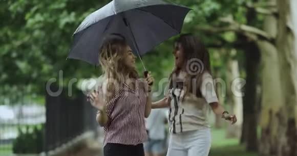 下雨天两位微笑的快乐女士在伞下跳跃4k缓慢的动作视频的预览图