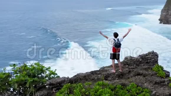 成功的青年男子剪影站在海洋悬崖高空举起武器快乐自由概念视频的预览图